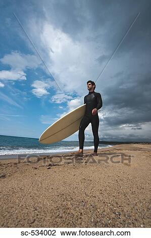 Surfer walking along the beach with his surfboard View Large Photo Image Stock Image - Surfer walking along the beach with his surfboard. Fotosearch