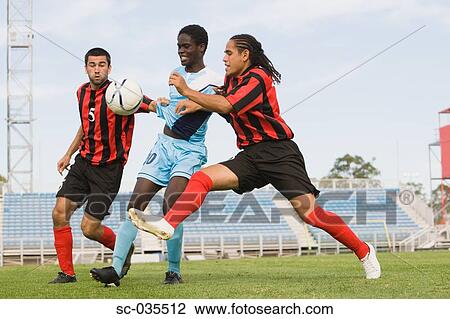 Stock Image - Three soccer players challenging for ball. Fotosearch