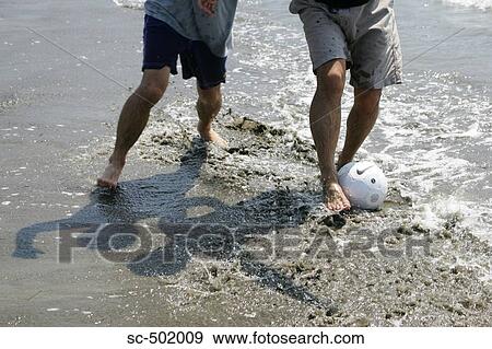 Stock Photo - Two Guys Playing Soccer In the Surf. Fotosearch