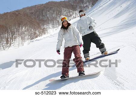 Stock Image - Two young Asian snowboarders looking at camera. Fotosearch