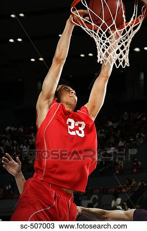Stock Image - Young Asian basketball player making a dunk. Fotosearch