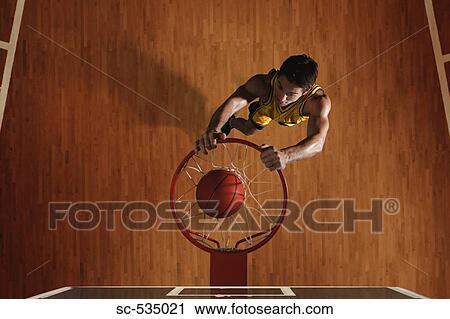 Stock Image - Young man dunking basketball in hoop. Fotosearch