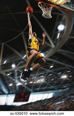 Stock Image - Young man holding basketball jumping in air. Fotosearch