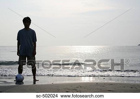 Picture - Young Man Posing With A Soccer Ball on the Beach. Fotosearch