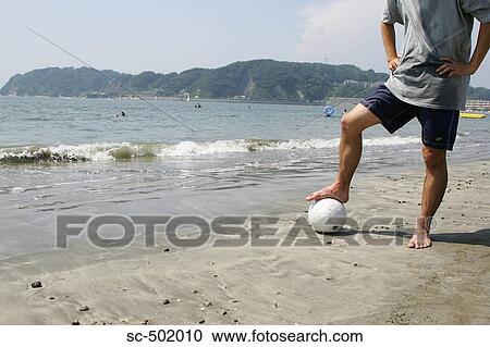 Stock Image - Young Man Posing With A Soccer Ball on the Beach. Fotosearch