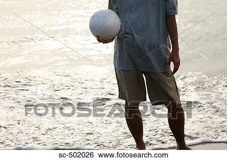 Stock Photograph - Young Man Posing With A Soccer Ball on the Beach. Fotosearch