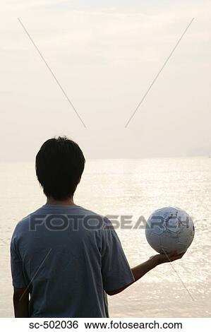 Stock Photograph - Young Man Posing With A Soccer Ball on the Beach. Fotosearch