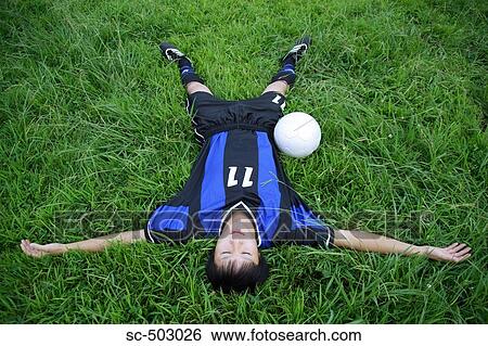 Stock Photograph - Young Man Sleeping Next To A Soccer Ball In a Field. Fotosearch