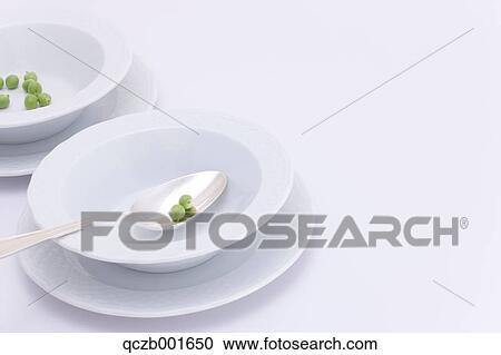 Stock Image - Green peas spoon and white plates . Fotosearch