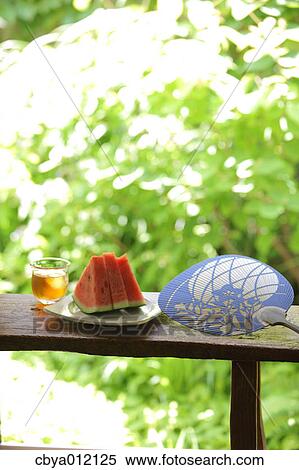 Stock Photography - Watermelon drink and paper fan on a wooden bench. Fotosearch