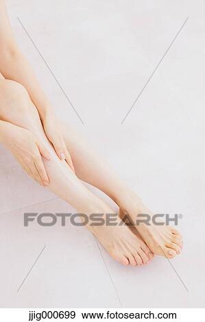 Stock Photo - Woman massaging her legs on the floor. Fotosearch