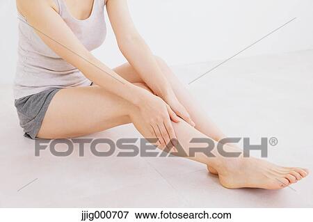 Stock Photo - Woman massaging her legs on the floor. Fotosearch