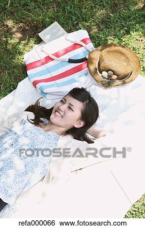 Stock Photograph - Young woman laying on grassland smiling. Fotosearch