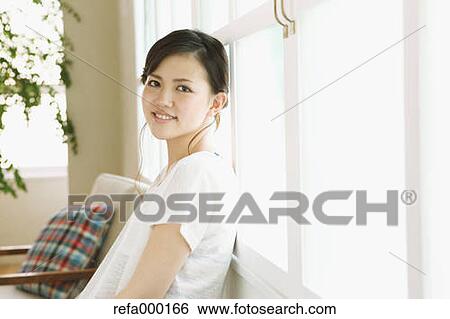 Young woman leaning by the window smiling View Large Photo Image Stock Photograph - Young woman leaning by the window smiling. Fotosearch