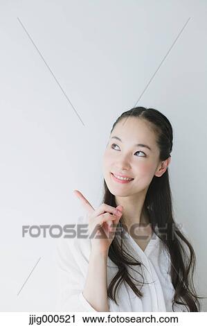 Stock Image - Young woman pointing finger up smiling. Fotosearch