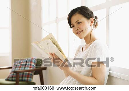 Stock Photo - Young woman reading a book by the window. Fotosearch