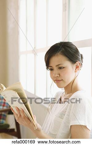 Young woman reading a book by the window View Large Photo Image Stock Photo - Young woman reading a book by the window. Fotosearch