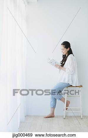 Stock Photo - Young woman sitting with book in the living room. Fotosearch