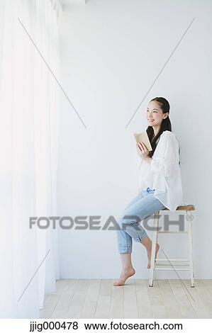 Stock Photo - Young woman sitting with book in the living room. Fotosearch