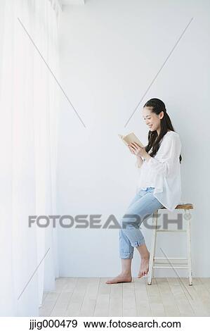 Stock Photo - Young woman sitting with book in the living room. Fotosearch