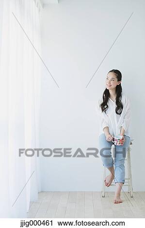 Young woman sitting with cup in the living room View Large Photo Image Stock Image - Young woman sitting with cup in the living room. Fotosearch
