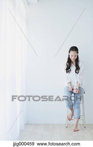 Young woman sitting with cup in the living room View Large Photo Image Stock Photo - Young woman sitting with cup in the living room. Fotosearch