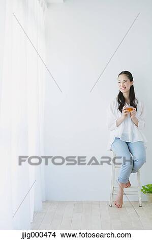 Young woman sitting with cup of tea in the living room View Large Photo Image Picture - Young woman sitting with cup of tea in the living room. Fotosearch