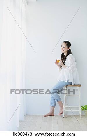 Young woman sitting with cup of tea in the living room View Large Photo Image Stock Image - Young woman sitting with cup of tea in the living room. Fotosearch