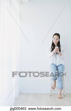 Stock Image - Young woman sitting with smart phone in the living room. Fotosearch