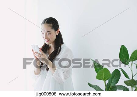 Young woman sitting with smart phone in the living room View Large Photo Image Stock Photo - Young woman sitting with smart phone in the living room. Fotosearch