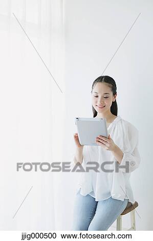 Stock Image - Young woman sitting with tablet in the living room. Fotosearch