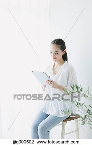 Young woman sitting with tablet in the living room View Large Photo Image Stock Image - Young woman sitting with tablet in the living room. Fotosearch