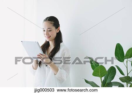 Stock Image - Young woman sitting with tablet in the living room. Fotosearch