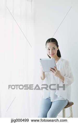 Young woman sitting with tablet in the living room View Large Photo Image Stock Photo - Young woman sitting with tablet in the living room. Fotosearch