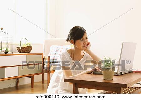 Stock Image - Young woman using PC in the living room. Fotosearch