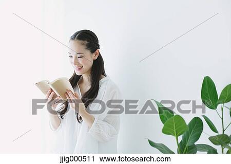 Stock Image - Young woman with book in the living room. Fotosearch