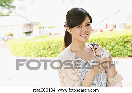 Young woman with smart phone smiling away View Large Photo Image Picture - Young woman with smart phone smiling away. Fotosearch