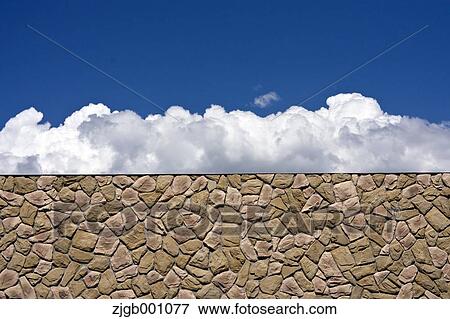Stock Photo - Stone wall and blue sky with clouds. Fotosearch