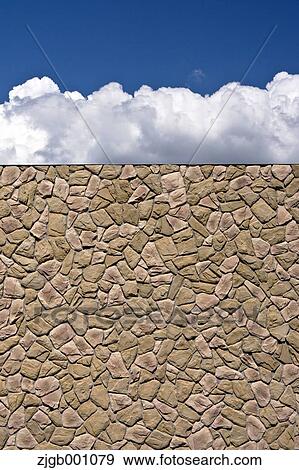 Stock Photo - Stone wall and blue sky with clouds. Fotosearch