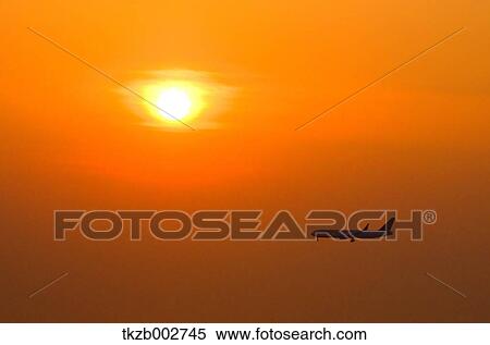 Stock Photography - Airplane flying on sunset sky. Fotosearch