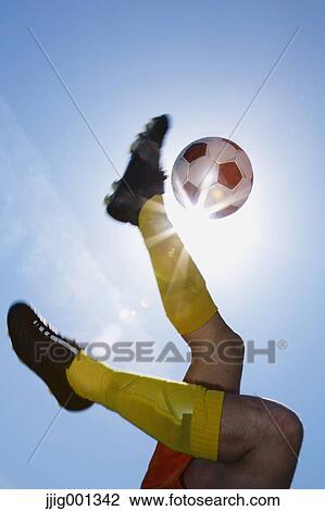 Stock Image - Football player kicking ball in mid-air. Fotosearch