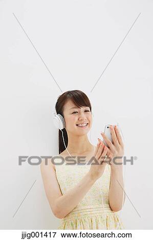 Stock Photo - Japanese young woman in a one piece dress with earphones standing against white background. Fotosearch
