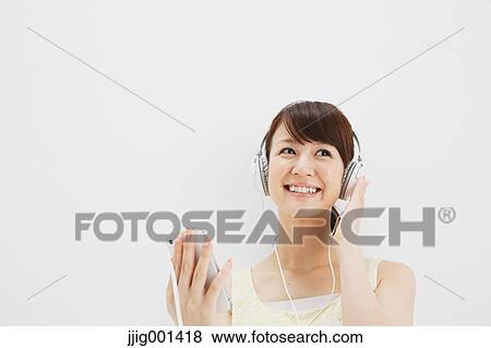 Stock Photo - Japanese young woman in a one piece dress with earphones standing against white background. Fotosearch