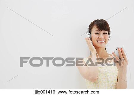 Japanese young woman in a one piece dress with earphones standing against white background View Large Photo Image Stock Photograph - Japanese young woman in a one piece dress with earphones standing against white background. Fotosearch