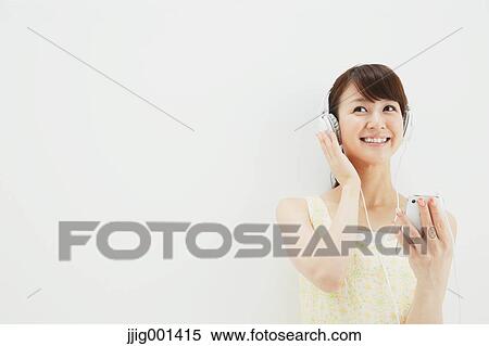 Stock Photography - Japanese young woman in a one piece dress with earphones standing against white background. Fotosearch