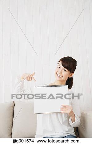 Picture - Japanese young woman in a white shirt with sketchbook on the sofa. Fotosearch