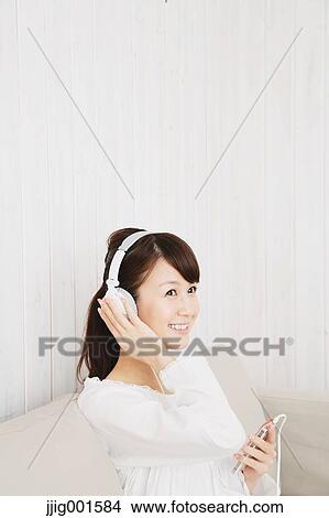 Japanese young woman in a white shirt with earphones on the sofa View Large Photo Image Picture - Japanese young woman in a white shirt with earphones on the sofa. Fotosearch