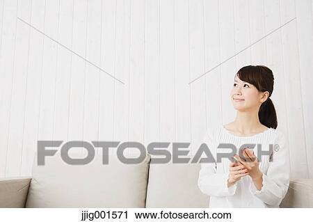 Japanese young woman in a white shirt with smartphone on the sofa View Large Photo Image Stock Image - Japanese young woman in a white shirt with smartphone on the sofa. Fotosearch