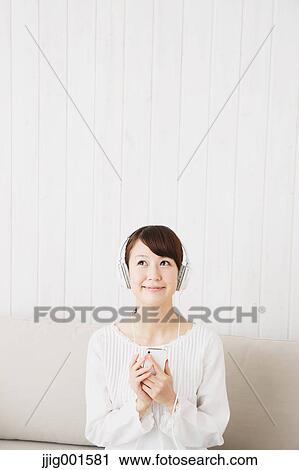 Japanese young woman in a white shirt with earphones on the sofa View Large Photo Image Stock Image - Japanese young woman in a white shirt with earphones on the sofa. Fotosearch