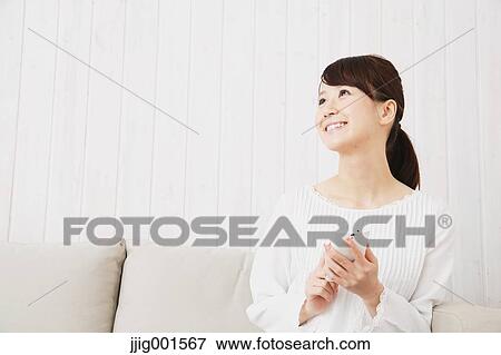 Japanese young woman in a white shirt with smartphone on the sofa View Large Photo Image Stock Photo - Japanese young woman in a white shirt with smartphone on the sofa. Fotosearch